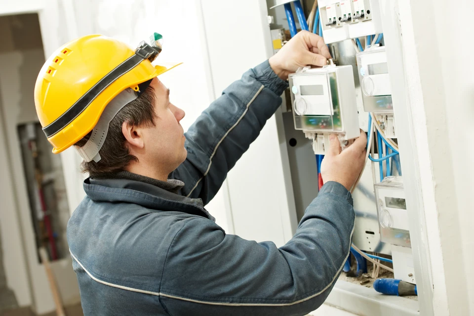 Technicien en casque jaune travaillant sur tableau électrique résidentiel, effectuant maintenance ou installation
