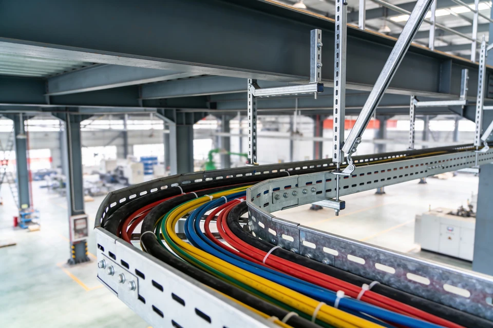 Scène d'atelier avec mains expertes manipulant un connecteur électronique multicolore à l'aide d'une pince de précision