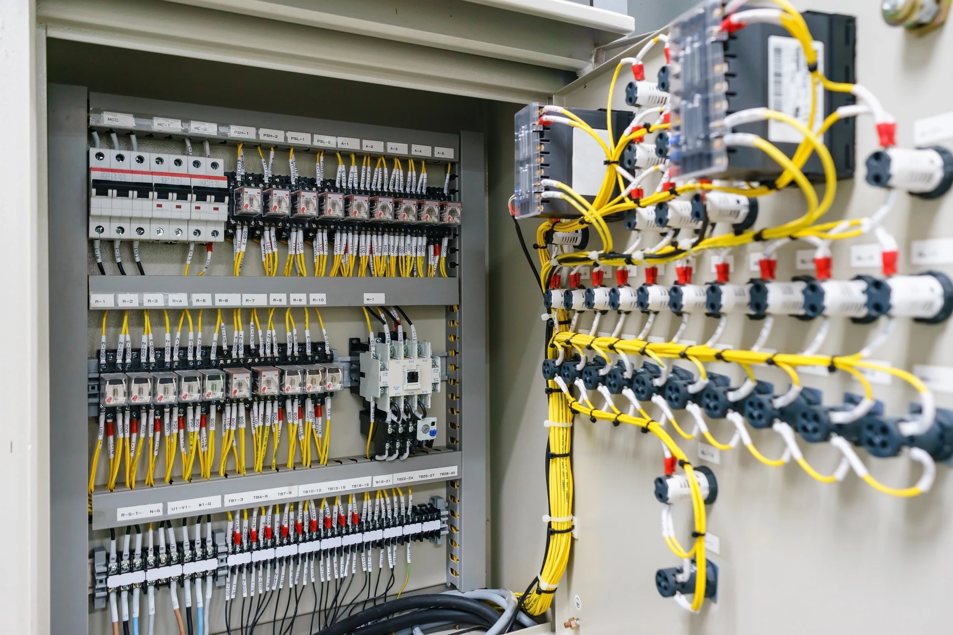 Technicien en combinaison travaillant sur panneau électrique industriel, manipulation de câbles avec outil de précision